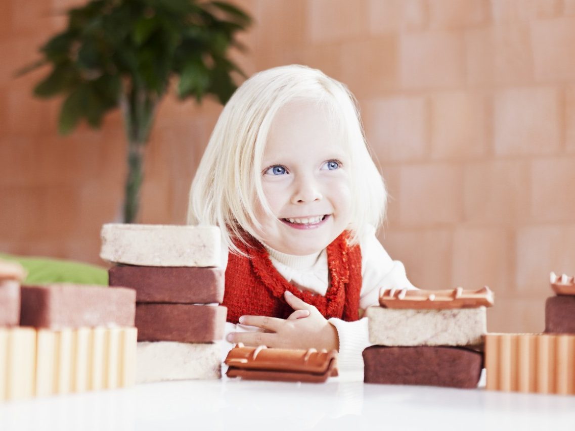 Young smiling girl with mini bricks and bare clay block wall in background