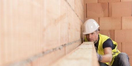 Construction worker checking alignment of mineral-wool filled clay block