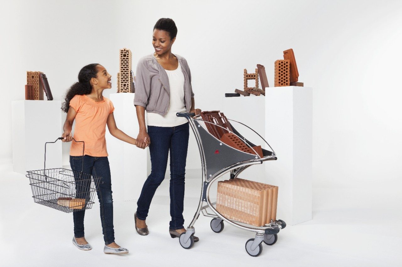 Girl with shopping basket and woman with shopping cart passing  by a selection of Wienerberger clay building materials