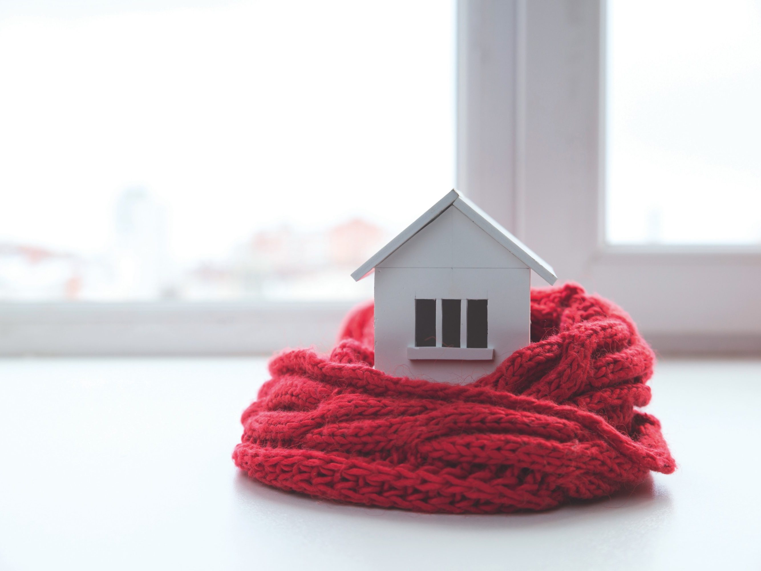 house in winter - heating system concept and cold snowy weather with model of a house wearing a knitted cap.