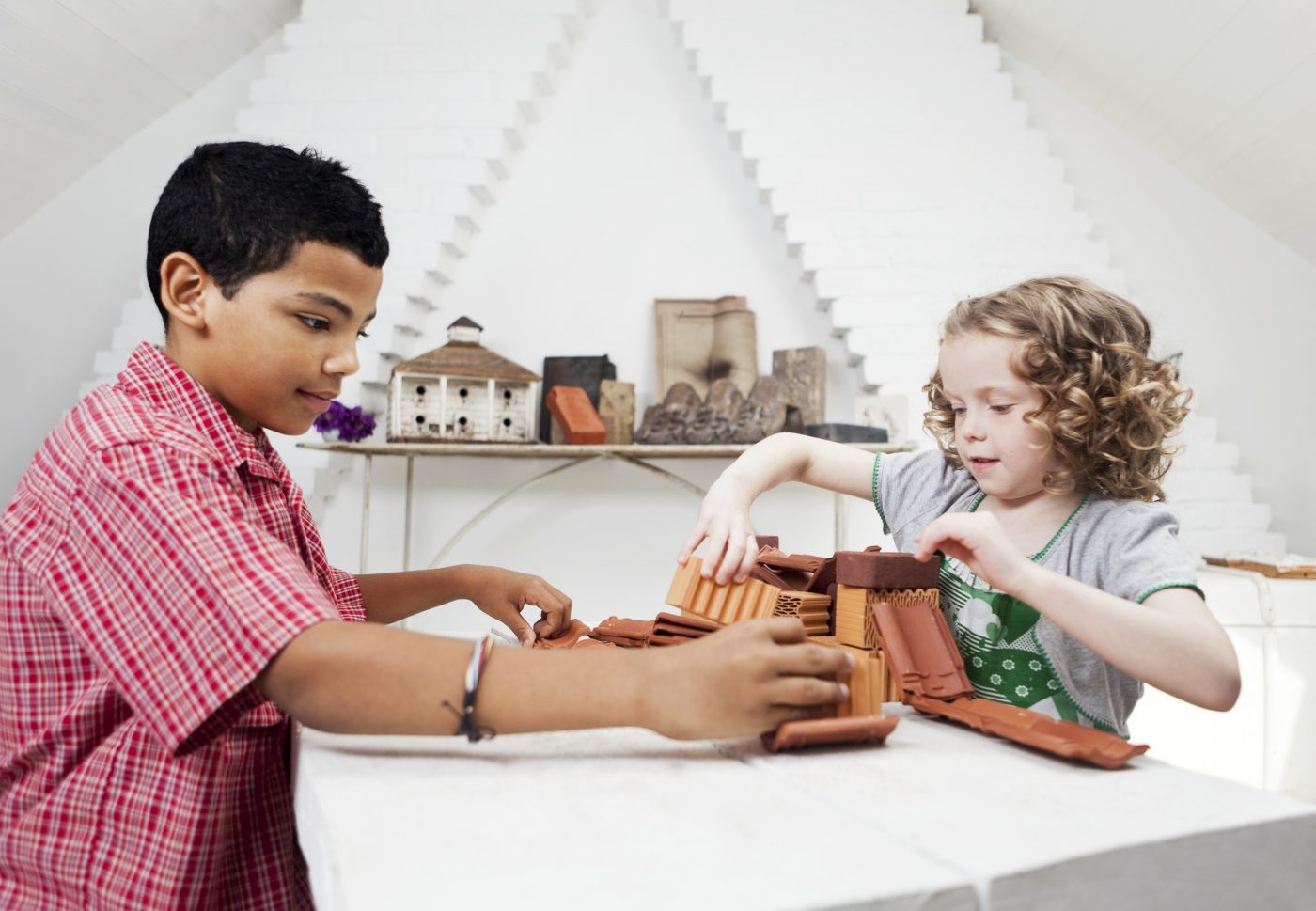 Boy and girl playing with miniature bricks, clay blocks and clay roof tiles in attic loft